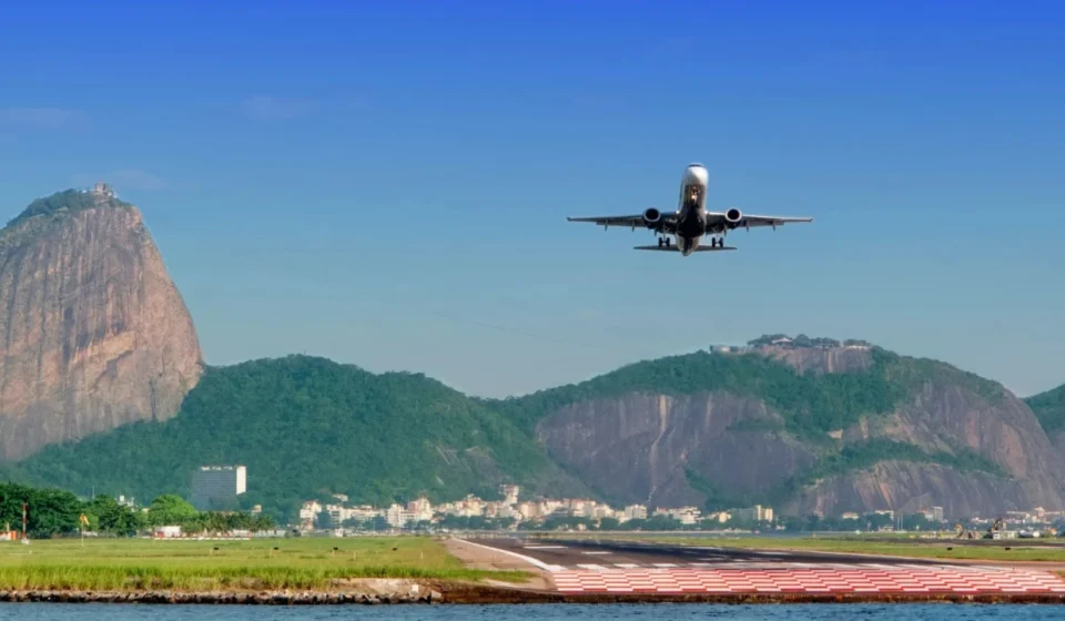 Passenger plane approaches a runway with Rio de Janeiro's mountains and waterfront clearly in view.