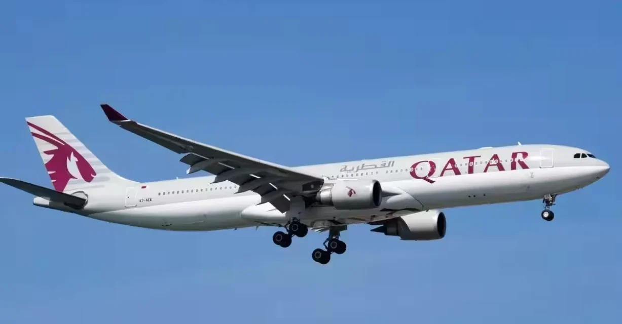 Qatar Airways passenger aircraft approaching for landing under a clear blue sky with landing gear deployed safely.