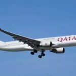 Qatar Airways passenger aircraft approaching for landing under a clear blue sky with landing gear deployed safely.