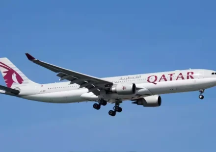 Qatar Airways passenger aircraft approaching for landing under a clear blue sky with landing gear deployed safely.