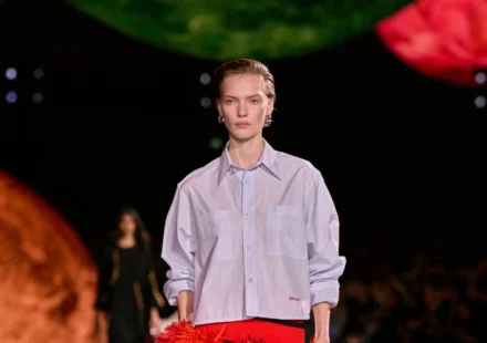 Model walks runway in a striped Chanel shirt during a fashion show showcasing the brand’s chic style.