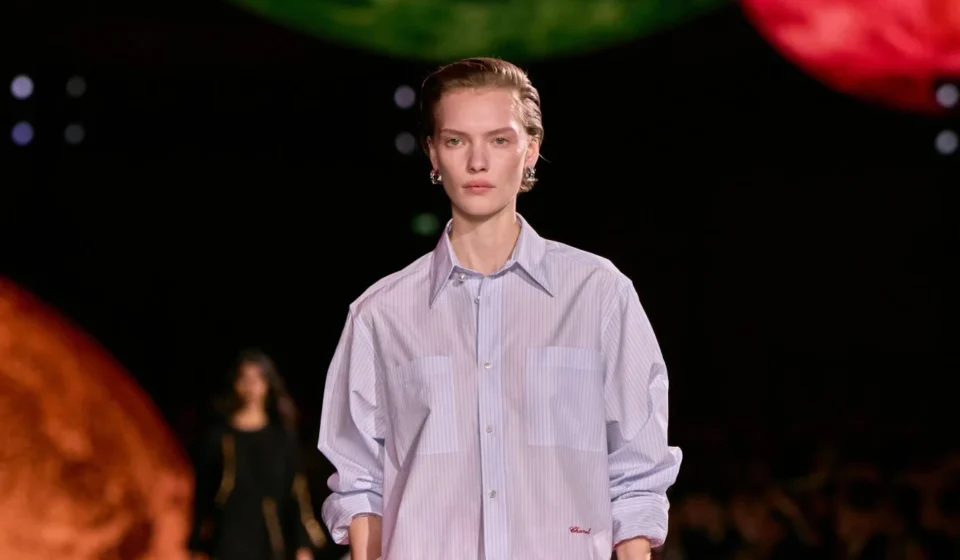 Model walks runway in a striped Chanel shirt during a fashion show showcasing the brand’s chic style.