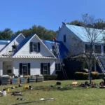 Workers repair a suburban home's roof as construction materials and ladders surround this property.