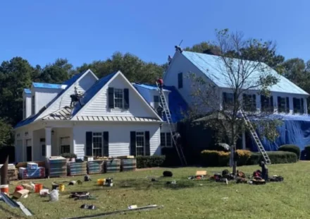 Workers repair a suburban home's roof as construction materials and ladders surround this property.
