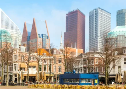 Modern commercial district with historic buildings, cafes, and tall towers beneath a clear blue sky.