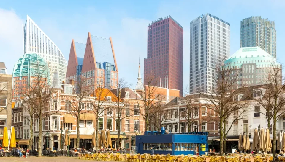 Cross-Border Commercial Real Estate Accord Standardizes ESG Valuations Modern commercial district with historic buildings, cafes, and tall towers beneath a clear blue sky.