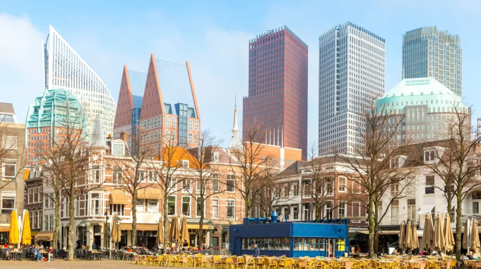 Modern commercial district with historic buildings, cafes, and tall towers beneath a clear blue sky.