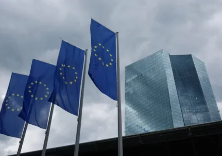 European Union flags fly outside the European Central Bank headquarters beneath dark clouds in Frankfurt, Germany.