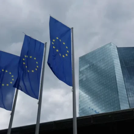 European Union flags fly outside the European Central Bank headquarters beneath dark clouds in Frankfurt, Germany.