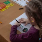 Ukrainian schoolgirl drawing at a desk during a lesson with pencils and materials nearby.