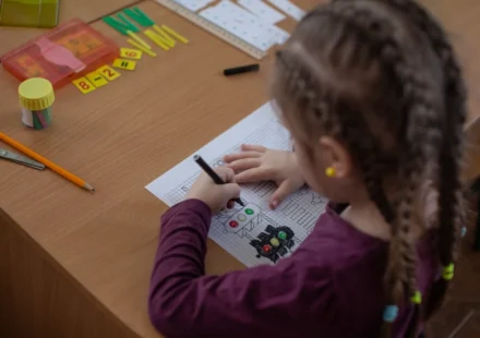 Ukrainian schoolgirl drawing at a desk during a lesson with pencils and materials nearby.