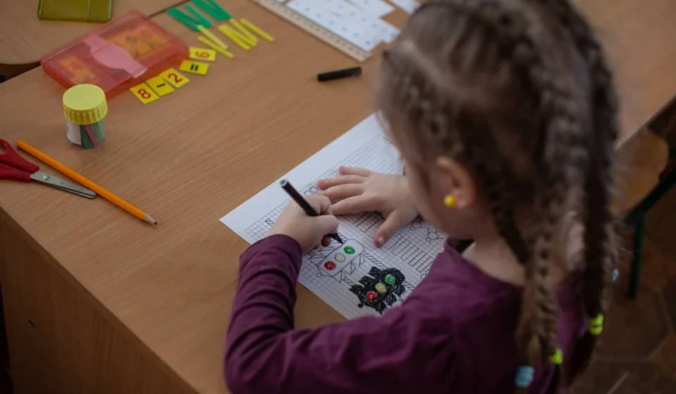Ukrainian schoolgirl drawing at a desk during a lesson with pencils and materials nearby.