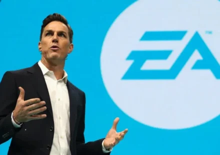 EA executive speaks on stage with the Electronic Arts logo displayed on a large screen behind him.