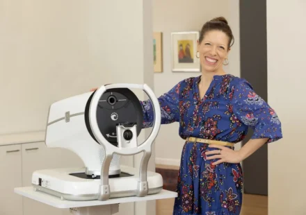 Woman standing beside advanced eye examination equipment in a clinic setting for glaucoma treatment.