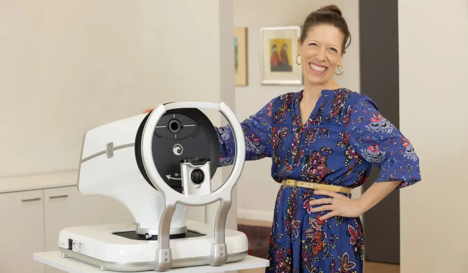 FDA Clears Advanced Glaucoma Surgical Device Woman standing beside advanced eye examination equipment in a clinic setting for glaucoma treatment.