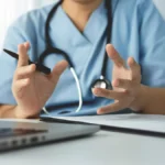 Doctor conducts a telehealth consultation while discussing patient care using a laptop and clipboard.