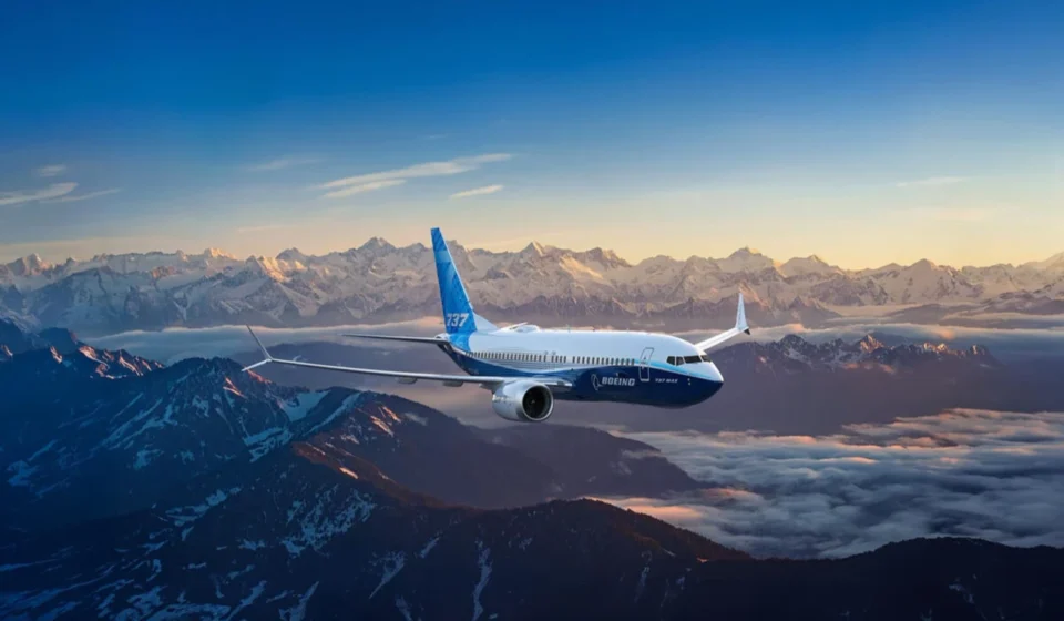 Boeing passenger jet flying above snow covered mountain peaks during sunrise with clear skies and clouds below