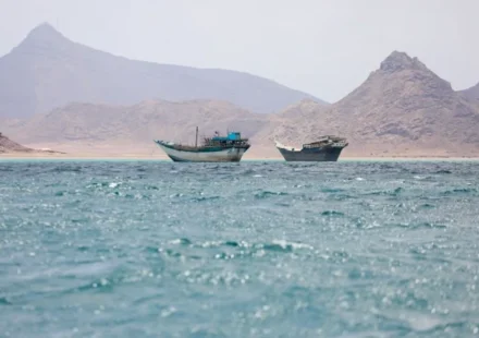 Boats on blue waters near rocky mountains in the Strait of Hormuz beneath hazy skies at daybreak sea