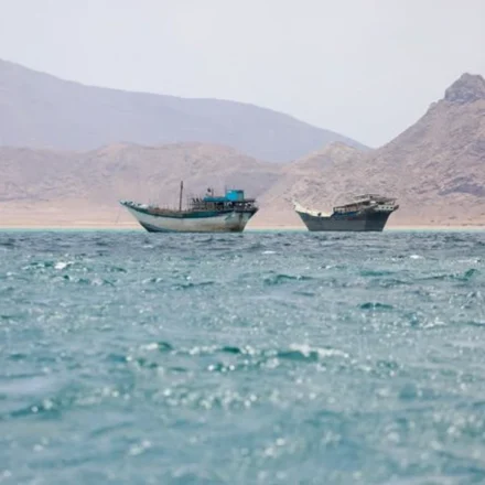 Boats on blue waters near rocky mountains in the Strait of Hormuz beneath hazy skies at daybreak sea