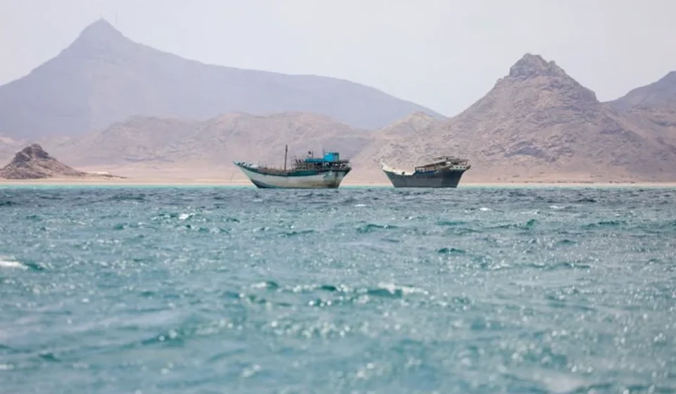 Gulf Shipping Traffic Drops Sharply After Maritime Chokepoint Attacks Boats on blue waters near rocky mountains in the Strait of Hormuz beneath hazy skies at daybreak sea