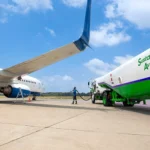 Airliner being refueled with sustainable aviation fuel from a green tanker at an airport apron today