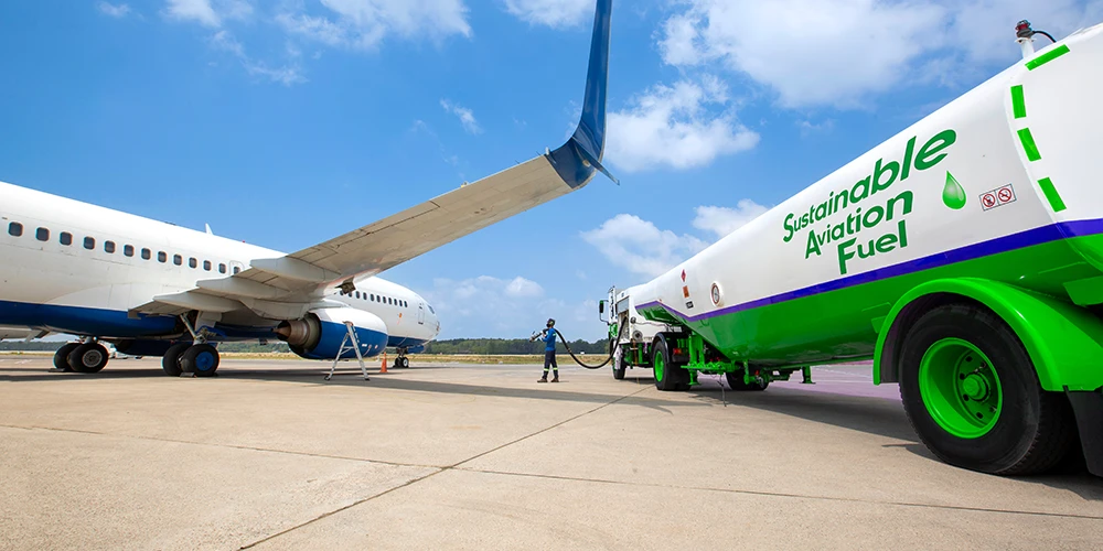Airliner being refueled with sustainable aviation fuel from a green tanker at an airport apron today