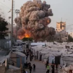 Smoke rises over tents in Gaza as explosion erupts near people seeking shelter nearby amid conflict.