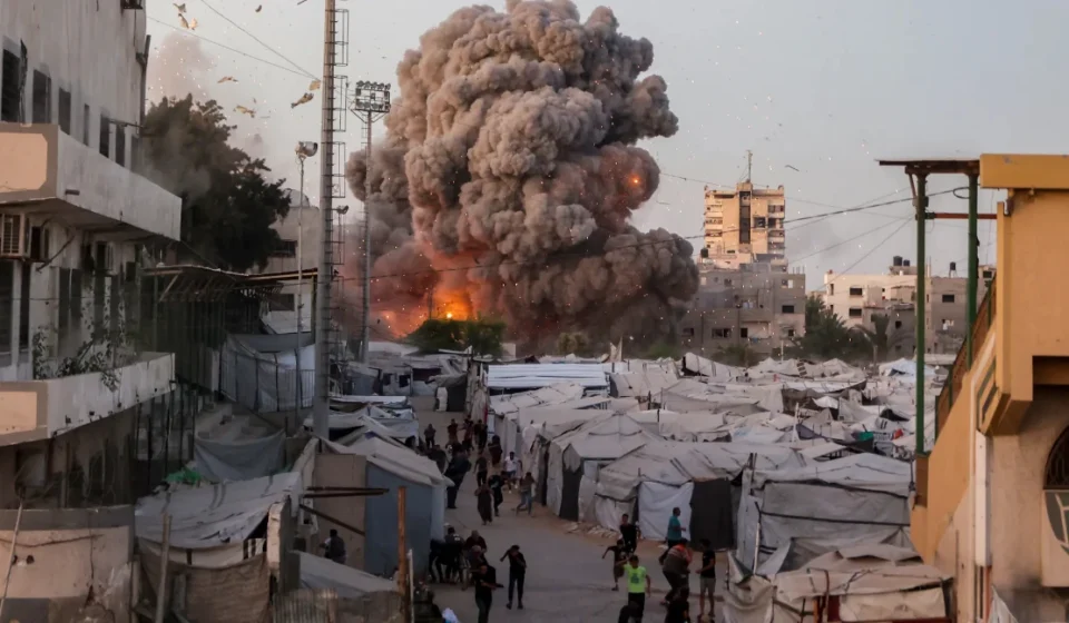 Israel Strikes Gaza Following Hamas Phased Disarmament Agreement Smoke rises over tents in Gaza as explosion erupts near people seeking shelter nearby amid conflict.