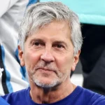 Jorge Messi watches from the stands at a football match, wearing a blue shirt, gray hair and beard.