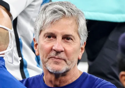 Jorge Messi watches from the stands at a football match, wearing a blue shirt, gray hair and beard.
