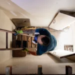 Worker climbs an attic ladder inside a home, highlighting risks linked to recalled stairway hardware