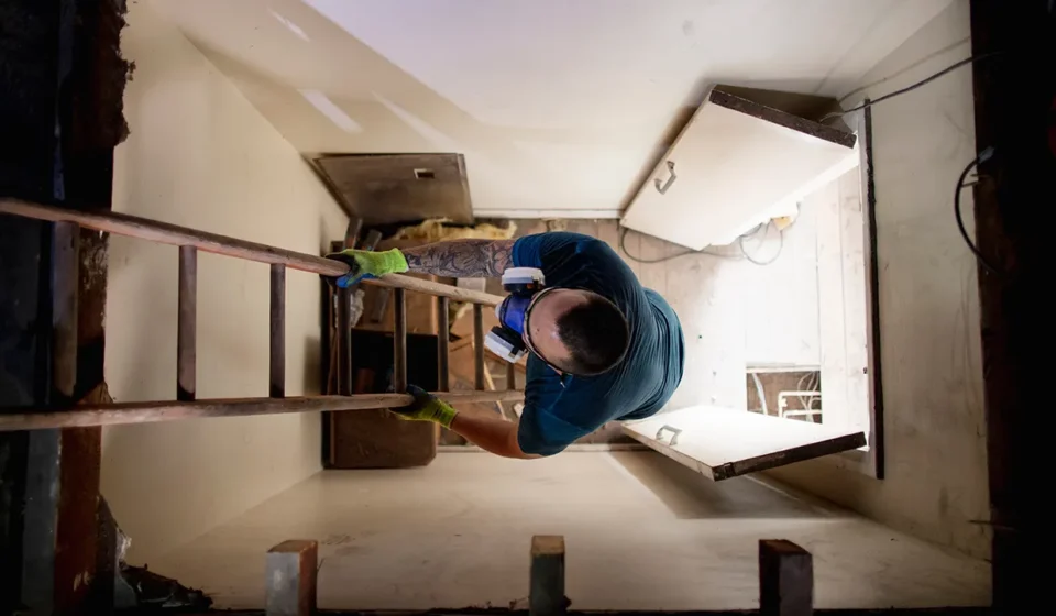 Worker climbs an attic ladder inside a home, highlighting risks linked to recalled stairway hardware