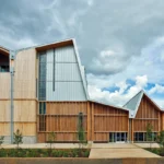 Modern mass timber building with engineered wood facade under dramatic clouds showcasing sustainable architecture design.