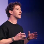 Meta executive speaking onstage in a black shirt, gesturing with both hands against a dark backdrop.