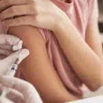 Young person receiving a meningitis vaccine in the upper arm during an NHS immunization appointment at clinic.