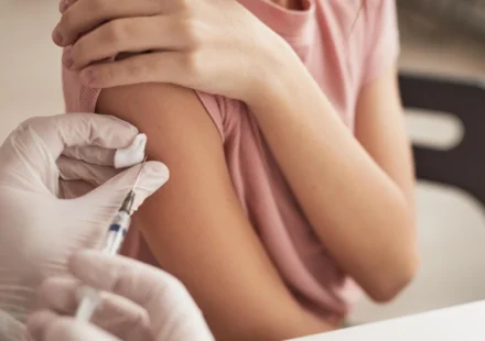 Young person receiving a meningitis vaccine in the upper arm during an NHS immunization appointment at clinic.