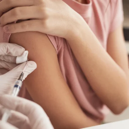 Young person receiving a meningitis vaccine in the upper arm during an NHS immunization appointment at clinic.