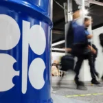 OPEC logo on blue oil barrel as attendees walk past during energy meeting after output increase. now