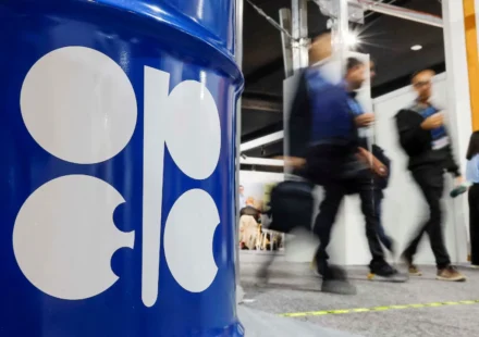 OPEC logo on blue oil barrel as attendees walk past during energy meeting after output increase. now