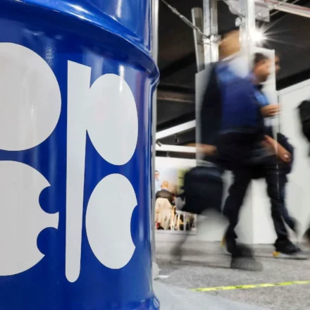 OPEC logo on blue oil barrel as attendees walk past during energy meeting after output increase. now