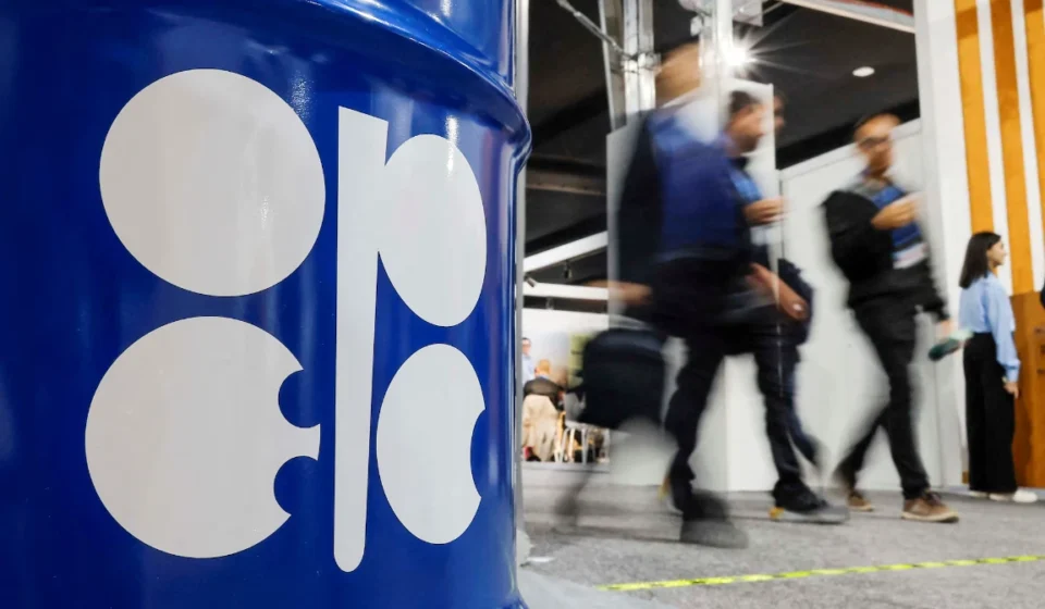 OPEC logo on blue oil barrel as attendees walk past during energy meeting after output increase. now