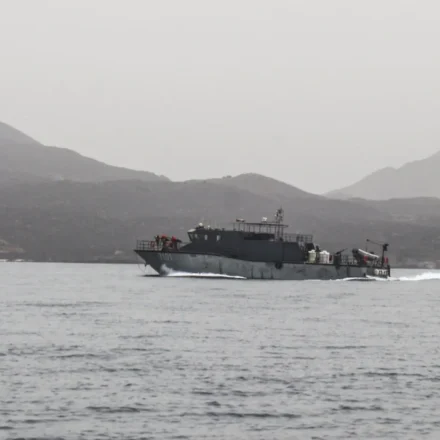 Naval patrol vessel speeds across calm Red Sea waters with rugged mountains in the distant background
