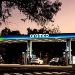 Aramco fuel station at dusk with cars refueling beneath illuminated canopy amid calm evening skyline.