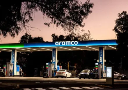Aramco fuel station at dusk with cars refueling beneath illuminated canopy amid calm evening skyline.