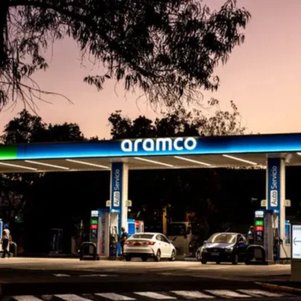 Aramco fuel station at dusk with cars refueling beneath illuminated canopy amid calm evening skyline.