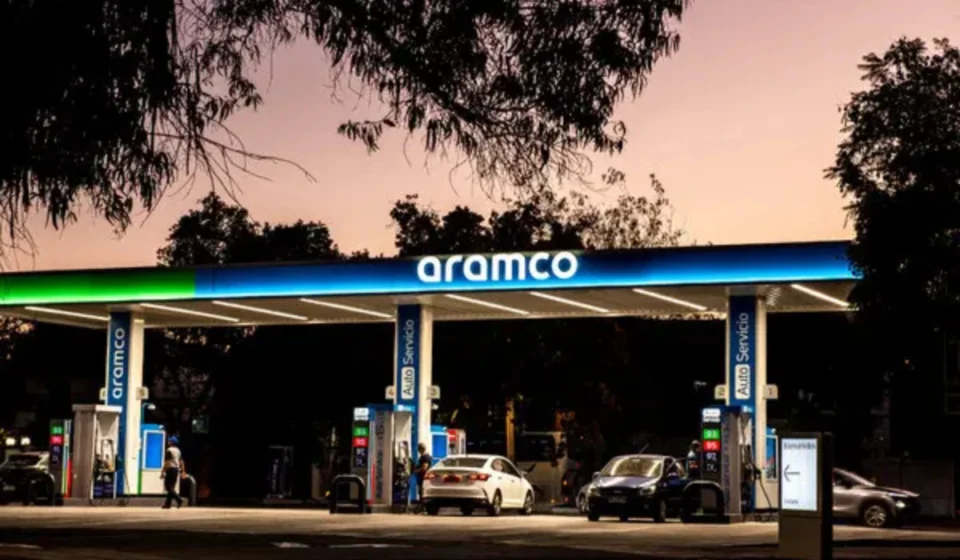 Aramco fuel station at dusk with cars refueling beneath illuminated canopy amid calm evening skyline.