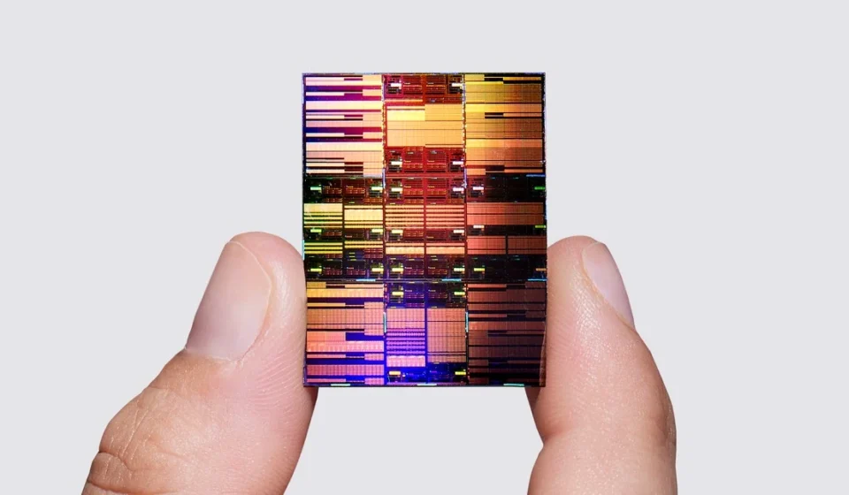 A semiconductor chip held between fingers displays a detailed multicolored circuit pattern up close.