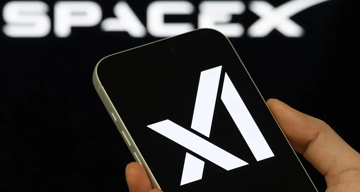 Hand holding smartphone showing Anthropic logo with blurred SpaceX branding in background during AI.