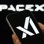 Hand holding smartphone showing Anthropic logo with blurred SpaceX branding in background during AI.