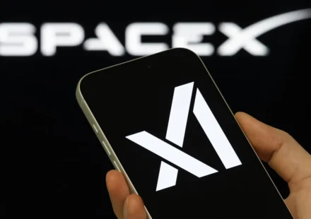 Hand holding smartphone showing Anthropic logo with blurred SpaceX branding in background during AI.